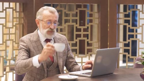 Old Businessman with Laptop at Coffee Break in His Office Concept