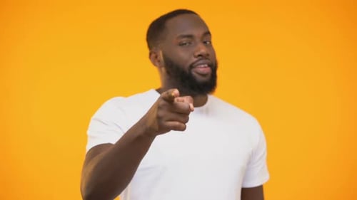 Man Points Finger and Winks on Orange Background
