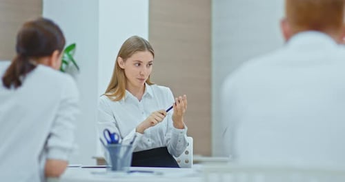Pretty Young Woman is Working in a Modern Office Sitting at a Table and Talking to Colleagues