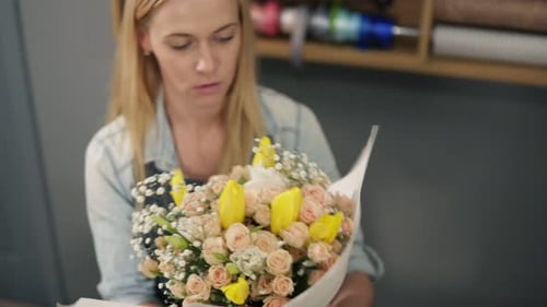 Jeune fleuriste blonde enveloppant un bouquet de fleurs dans du papier décoratif