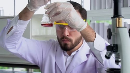 Scientist Analyzing Red Liquid in Laboratory Beaker