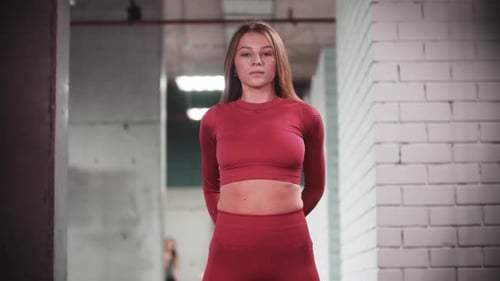 Young Woman in Red Sports Suit Doing Fitness Exercises in the Gym Looks in the Camera and Bending