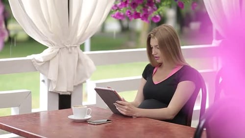 Beautiful girl with light hair wearing colorful shirt sitting in cafe with tablet