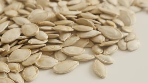 Raw organic pepitas close-up slow tilt 4K 2160p 30fps UltraHD footage - Pile of pumpkin seed on whi