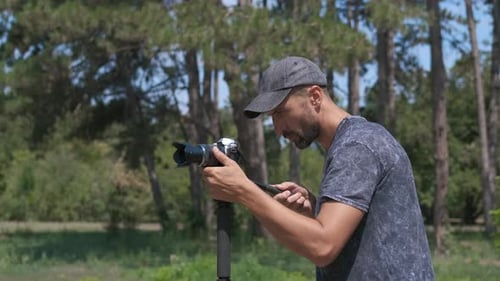 Smiling Man Adjusts Camera in a Forest