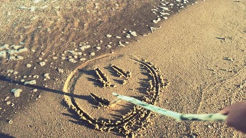 Stick Draws Smiley Face on Sandy Beach