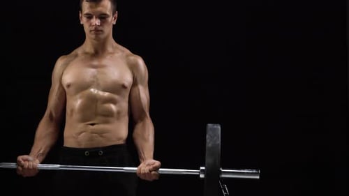 Man is Doing Exercises with a Barbell Training on a Black Background in the Studio