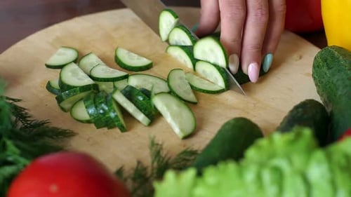 Woman Slicing Fresh Cucumber on Wooden Board