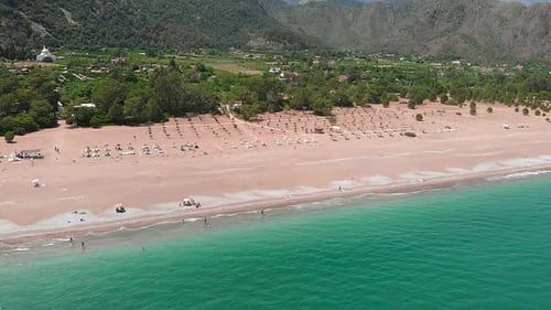 Tropical island with wide crowded sandy beach and mountain hills.