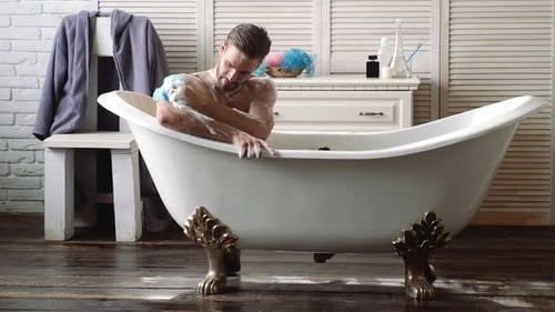 Man Soaking in Bathtub with Soap and Sponge