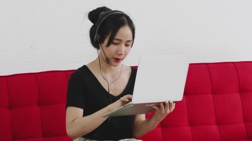 Woman Using Laptop Computer with Headset on Couch