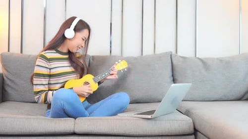 Woman Plays Ukulele on Couch with Laptop