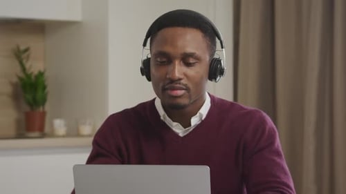 Man Puts on Headphones and Works on Laptop