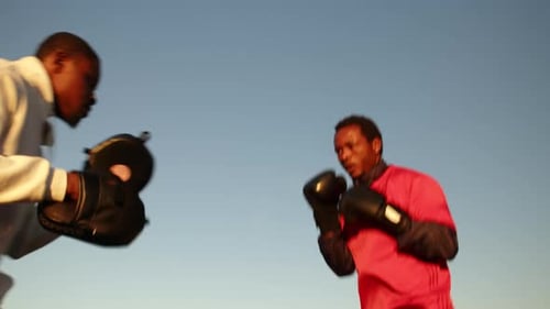 Black Man in Sportswear is Boxing with His Trainer Outdoors Side View
