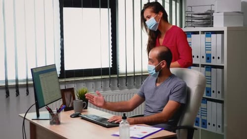 Man and Woman Discuss Computer in Office with Masks