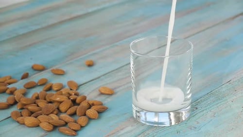 Pouring Almond Milk Into Glass with Almonds