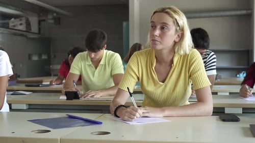 Junges blondes Mädchen hört sich eine Vorlesung an und schreibt Notizen in einem Klassenzimmer