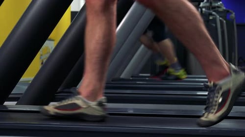 A Fit Man Walks on a Treadmill in a Gym - Side Closeup on the Feet