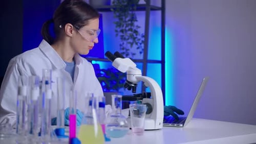 Scientist Uses Microscope and Laptop in Lab