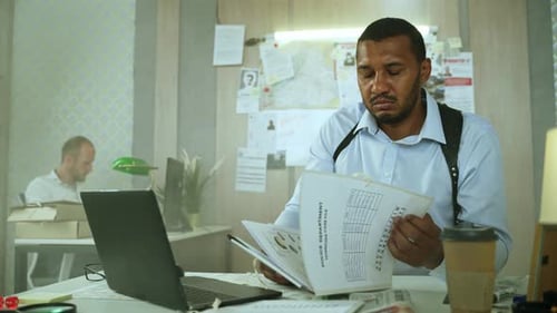 Detective Reviews Documents on Laptop in Office