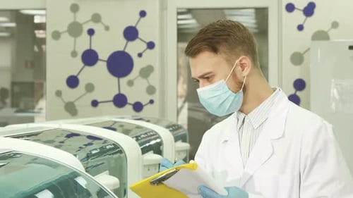 Man Writes on Clipboard in Bright Modern Laboratory