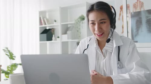 Young Asian lady doctor using computer laptop talking video call with patient in hospital