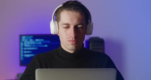 Close Up of Smiling Young Man in Headphones with Laptop Working at Night