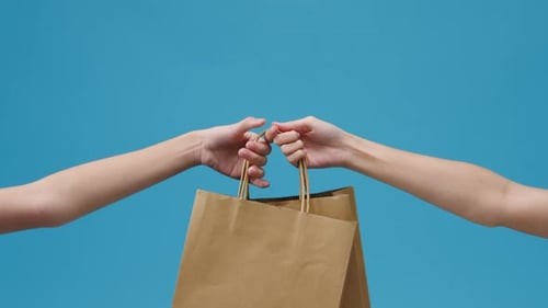 Hand Passing a Paper Bag to Another Hand
