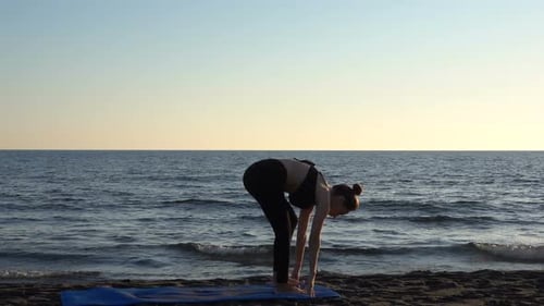 Young Caucasian Woman Practicing Yoga on the Beach Near Calm Sea, Sunrise Background.