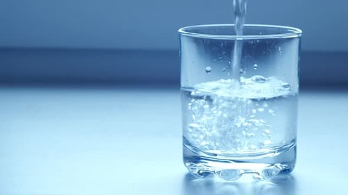 Clear Drinking Water Pouring Into Glass on Blue Grey Background. Mineral Water Pouring Into