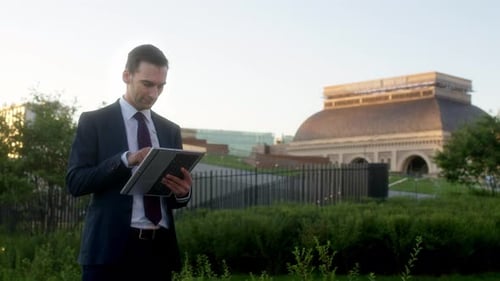 Serious Businessman Using Tablet Looks at Building in Background Turns Around and Shakes His Head in