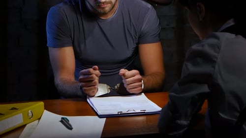 Man in Handcuffs Signs Document in Interrogation Room