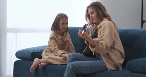Woman Playing Ukulele with Young Girl on Couch