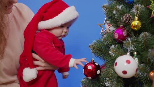 Baby Touches Christmas Ornament on Decorated Holiday Tree