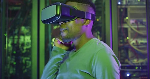 African american male computer technician using vr headset working in business server room