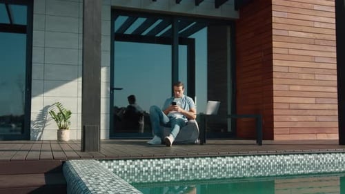 Man Using Mobile Phone by Modern Home Pool