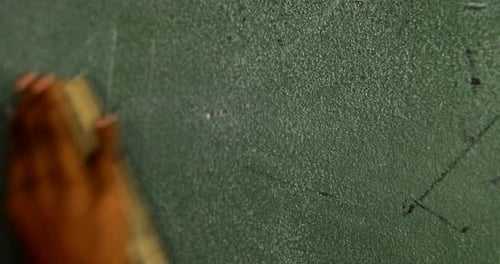 Mano de un colegial frotando la pizarra con un plumero en el aula