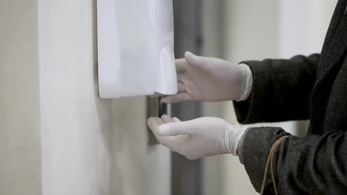 Adult Using Hand Sanitizer Dispenser with Gloves
