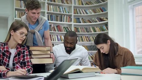 Multiracial Students Preparing for Exams in the Library while Their Friend Carring Other Books