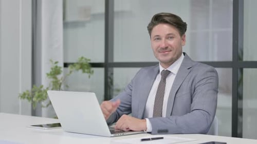 Confident Businessman Giving Thumbs Up at Office Desk