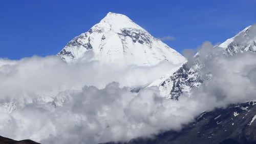Timelapse Clouds Swirl Over a Mountain Valley a Snowy Peak in the Distance