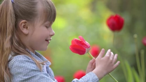 Jolie jeune fille jouant avec une fleur de tulipe rouge en été à l'extérieur.