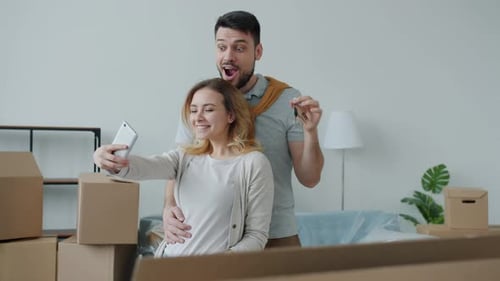 Young Man and Woman Taking Selfie with Keys To New Apartment Using Smartphone Camera