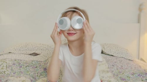 Girl Plays with Headphones on Bed Indoors