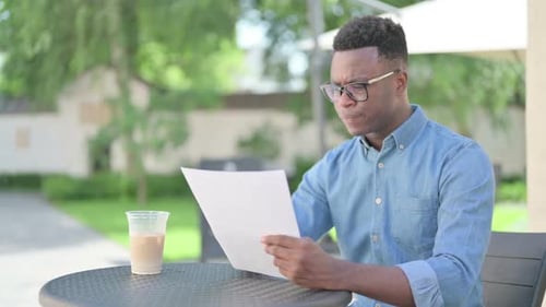 Frustrated Young Adult Looks at Papers Outdoors