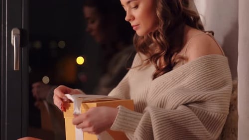Woman Opens Gift by Window at Night