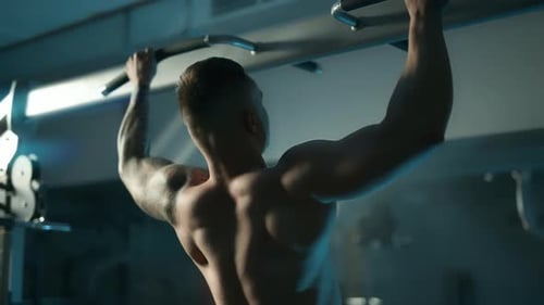 A Handsome Young Muscular Sportsman is Doing Exercise on a Fitness Machine in the Gym