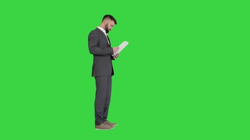 Businessman Standing and Reading Docs Seriously on a Green Screen, Chroma Key.
