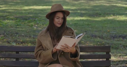Woman Reading a Book on Park Bench in Autumn