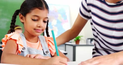 Teacher helping schoolgirl with their homework in classroom